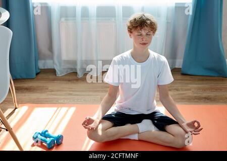 Junge kaukasische Teenager Jungen Sport zu Hause ausüben, Yoga üben, sitzen in Pose, Ruhe zu halten, meditieren Stockfoto