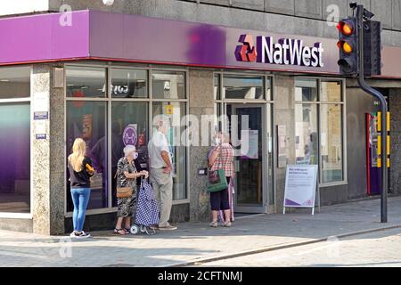 Covid 19 Gesichtsmaske von Nat West Bank Outdoor getragen Soziale Distanzierung von Kunden in der Warteschlange, um in die Coronavirus-Pandemie der Zweigstelle einzutreten Brentwood Essex England Großbritannien Stockfoto