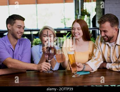 Gruppe von Freunden klirken Gläser mit Getränken im Café, junge Männer und Frauen versammelten sich, um Spaß zu haben und zu reden, Nachrichten zu teilen Stockfoto