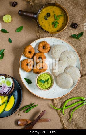 Draufsicht auf Idli, Wada, Sambar und Chutney. Traditionelle südindische Küche, umgeben von Zitrone, roher Mango und grünen Chilischoten. Stockfoto