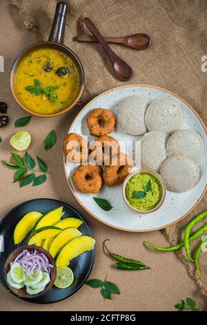 Draufsicht auf Idli, Wada, Sambar und Chutney. Traditionelle südindische Küche, umgeben von Zitrone, roher Mango und grünen Chilischoten. Stockfoto