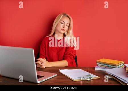 Porträt der jungen kaukasischen blonde Frau am Arbeitsplatz, sitzt sie in lässiger Kleidung am Schreibtisch, genießen Sie die Arbeit auf Laptop und mit Dokumenten. Isoliert Stockfoto