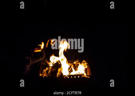 Feuer auf einem dunklen Hintergrund. Feuer aus Feuerholz aus der Nähe. Brennende Funken aus der Nähe, Brandmuster. Rot und orange Infernal Glut des Feuers in der da Stockfoto