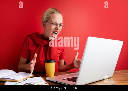 Wütend Frau ist in Schock bei der Arbeit, Blick auf Laptop unzufrieden. Isoliert roten Hintergrund Stockfoto