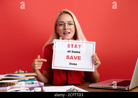 Selbstbewusste junge Dame bitten die Menschen, bei Freiberufler arbeiten, von zu Hause aus, zu Hause bleiben und das Leben zu retten, sie zeigt Finger auf Tablet. Frau am Schreibtisch, schauen Stockfoto