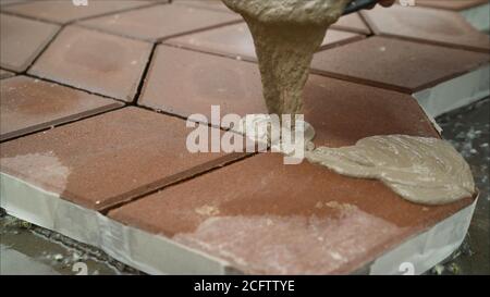Füllen von Pflasterplatten mit einer Lösung auf der Straße. Der Bauherr füllt die Nähte zwischen den Pflasterplatten. Stockfoto