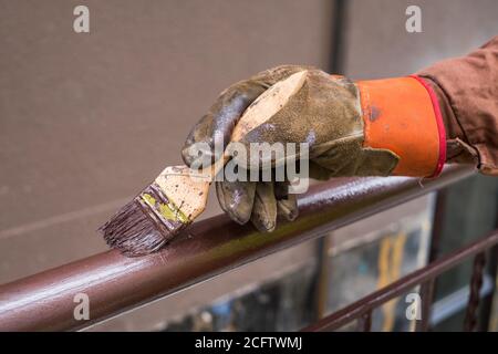 Hand des Auftragnehmers mit Pinsel, die Metallgeländerkonstruktion lackieren. Stockfoto