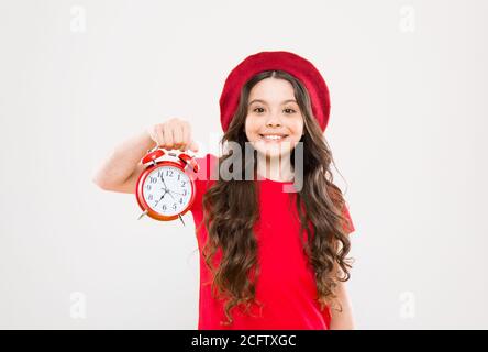 Shopping, Verkauf und Zeit Konzept. Pariser Kind auf Gelb. Kind mit Wecker. Zeitlose Mode. glückliches Mädchen mit langen Locken in Baskenmütze. Schönheit Friseur. Kleines Mädchen im französischen Stil hat. Stockfoto