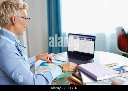 Blonde kaukasische weibliche junge Schullehrerin mit Webcam zu Hause, virtuelles Unterrichtskonzept, geben Remote-Klasse Online-Unterricht per Zoom Konferenzgespräch Stockfoto