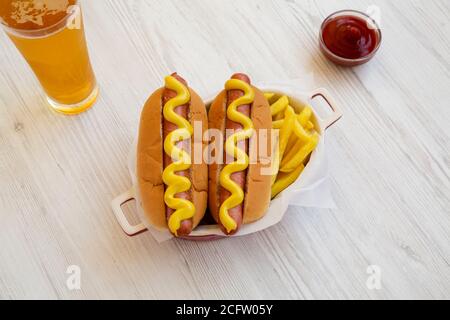 Hausgemachter Senf Hot Dog mit King Pommes und einem Glas kaltem Bier auf weißem Holzhintergrund, Blick in den hohen Winkel. Stockfoto