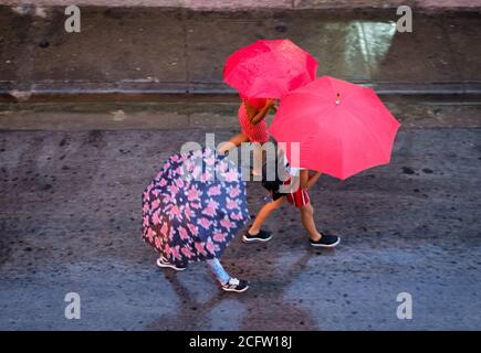 SANTIAGO DE CUBA, KUBA - CA. JANUAR 2020: Fußgänger, die an einem regnerischen Tag in Santiago de Cuba spazieren. Stockfoto