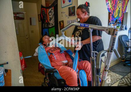 Sacramento, Kalifornien, USA. Februar 2020. FELICIA BRENT-VELASQUEZ teilt einen Lichtmoment mit ihrer Mutter FELICIA CLARK, während sie in ihrem Aufzug zu ihrem Rollstuhl in ihrem Haus in Sacramento gehisst wird. Clark hatte mehrere Stunden damit verbracht, sie anzuziehen, ihr Haar zu stylen, sie zu waschen, sie zu füttern, die Öffnung in ihrer Luftröhre zu saugen, als sie blockiert wurde, und dann sie in Decken gebündelt, um draußen zu gehen, um gegen das Kinderheim von Sacramento zu protestieren, wo sie einst lebte. Quelle: Renee C. Byer/Sacramento Bee/ZUMA Wire/Alamy Live News Stockfoto