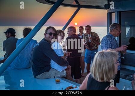 Ein Mann hält ein Mädchen in seinen Armen, während beide auf dem Deck der True North sitzen und den Sonnenuntergang vor den Sunda-Inseln, Indonesien, beobachten. Stockfoto