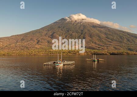 Der Vulkan Ile Lewotolok ragt über zwei Auslegerboote mit Hebenetzrahmen vor der Küste von Lembata, Indonesien, eine Wolke liegt über seinem Gipfel. Stockfoto