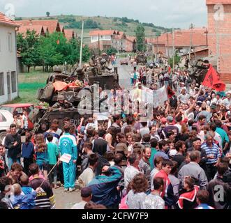 1999 - Ethenic Albaner versammeln sich in den Straßen für eine Parade statt die amerikanischen Streitkräfte im Kosovo Dorf Koretin zu ehren. Marines an Bord ihrer LAV-25, Leichte gepanzerte Fahrzeuge sind entlang der Straße Seite gesehen. Stockfoto