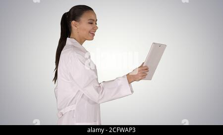 Junge Frau Arzt hält Tablet in den Händen und macht Video-Anruf auf Gradienten Hintergrund. Stockfoto