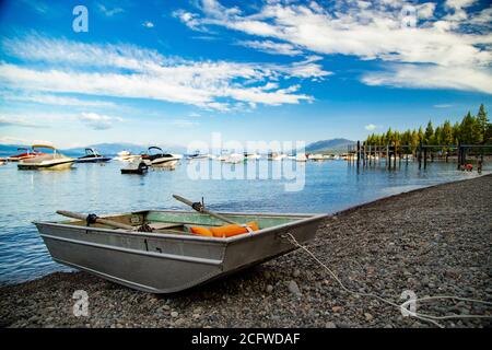 Altes Ruderboot aus Metall mit Rudern und orangefarbener Schwimmweste, hochgezogen auf felsigen Ballen am Rande des Lake Tahoe, Marina-Boote und Pier im Hintergrund Stockfoto