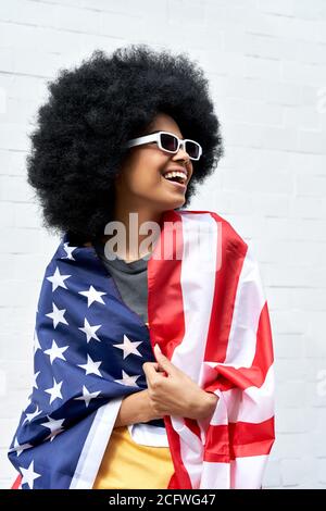 Glückliche junge afrikanische Frau eingewickelt in USA Flagge steht gegen weiße Wand. Stockfoto