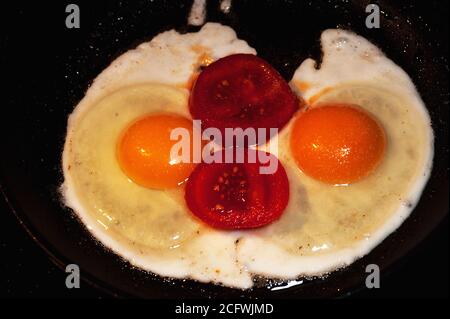 Kunstfoto von Spiegeleiern mit Tomatenscheiben gebraten in Butter in einer schwarzen Pfanne Stockfoto