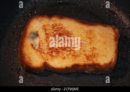 Kunstfoto von Croutons aus einer Scheibe Brot gebraten In Butter auf einer schwarzen Pfanne Stockfoto