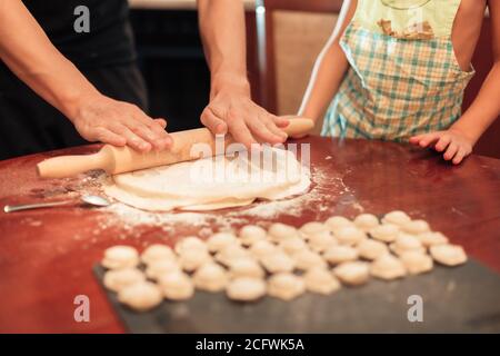 Mann rollt den Teig für Knödel aus. Kind in der Nähe hilft. Nahaufnahme Stockfoto