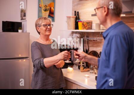 Reifes Paar, das einander ansieht und abends Gläser Rotwein hält. Gealtertes Paar in der Liebe zu sprechen angenehme Unterhaltung während einer gesunden Mahlzeit. Stockfoto