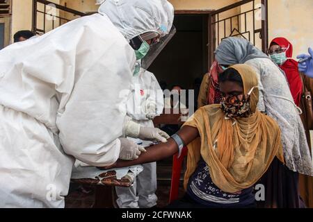 Lhokseumawe, Indonesien. September 2020. Ein Polizist, der einen Schutzanzug (PSA) trägt, nimmt Blut, um eine ethnische Rohingya-Frau in einem provisorischen Tierheim zu untersuchen.Fast 300 ethnische Rohingya-Muslime sind in den Gewässern des Aceh-Meeres gestrandet. Bestehend aus Erwachsenen und Kindern, die aufgrund von Austrocknung und Hunger schwach sind, nachdem sie auf hoher See beeinflusst wurden. Kredit: SOPA Images Limited/Alamy Live Nachrichten Stockfoto