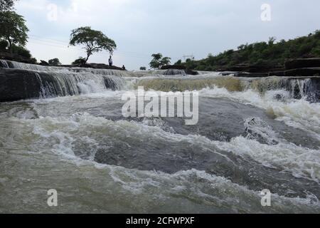 Bokeh-Aufnahme eines fließenden Wasserfalls mit selektivem Fokus und Baumhintergrund. Kleine Kinder baden im gefährlichen Wasserfall in Mirzapur, Indien w Stockfoto