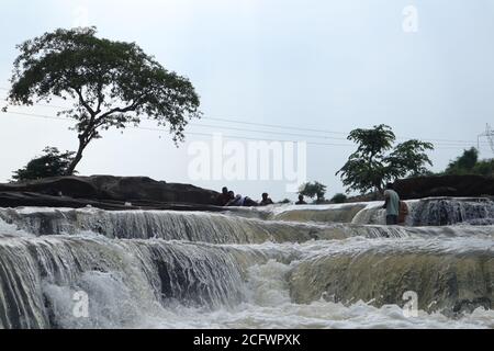 Bokeh-Aufnahme eines fließenden Wasserfalls mit selektivem Fokus und Baumhintergrund. Kleine Kinder baden im gefährlichen Wasserfall in Mirzapur, Indien w Stockfoto