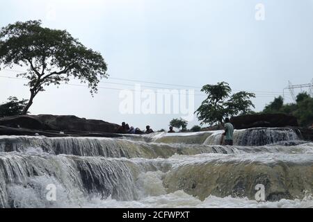 Bokeh-Aufnahme eines fließenden Wasserfalls mit selektivem Fokus und Baumhintergrund. Kleine Kinder baden im gefährlichen Wasserfall in Mirzapur, Indien w Stockfoto