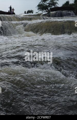 Bokeh-Aufnahme eines fließenden Wasserfalls mit selektivem Fokus und Baumhintergrund. Kleine Kinder baden im gefährlichen Wasserfall in Mirzapur, Indien w Stockfoto