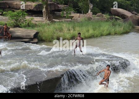 Bokeh-Aufnahme eines fließenden Wasserfalls mit selektivem Fokus und Baumhintergrund. Kleine Kinder baden im gefährlichen Wasserfall in Mirzapur, Indien w Stockfoto