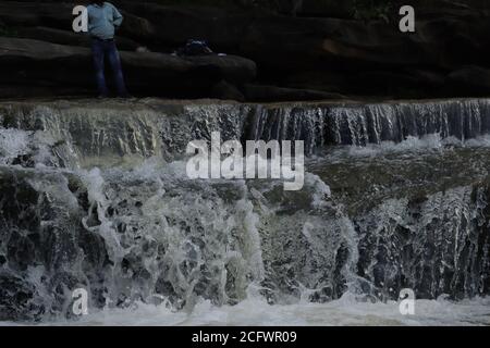 Bokeh-Aufnahme eines fließenden Wasserfalls mit selektivem Fokus und Baumhintergrund. Kleine Kinder baden im gefährlichen Wasserfall in Mirzapur, Indien w Stockfoto