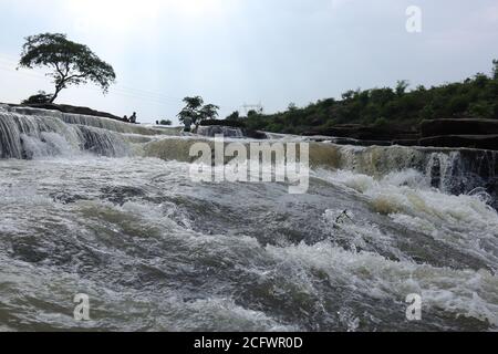 Bokeh-Aufnahme eines fließenden Wasserfalls mit selektivem Fokus und Baumhintergrund. Kleine Kinder baden im gefährlichen Wasserfall in Mirzapur, Indien w Stockfoto
