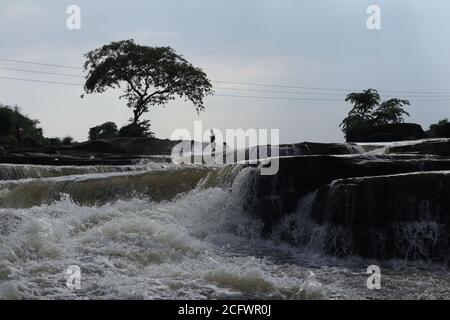 Bokeh-Aufnahme eines fließenden Wasserfalls mit selektivem Fokus und Baumhintergrund. Kleine Kinder baden im gefährlichen Wasserfall in Mirzapur, Indien w Stockfoto