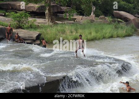 Bokeh-Aufnahme eines fließenden Wasserfalls mit selektivem Fokus und Baumhintergrund. Kleine Kinder baden im gefährlichen Wasserfall in Mirzapur, Indien w Stockfoto
