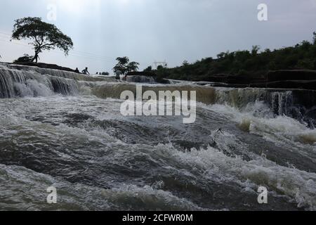 Bokeh-Aufnahme eines fließenden Wasserfalls mit selektivem Fokus und Baumhintergrund. Kleine Kinder baden im gefährlichen Wasserfall in Mirzapur, Indien w Stockfoto