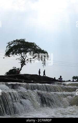 Bokeh-Aufnahme eines fließenden Wasserfalls mit selektivem Fokus und Baumhintergrund. Kleine Kinder baden im gefährlichen Wasserfall in Mirzapur, Indien w Stockfoto