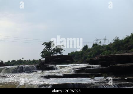 Bokeh-Aufnahme eines fließenden Wasserfalls mit selektivem Fokus und Baumhintergrund. Kleine Kinder baden im gefährlichen Wasserfall in Mirzapur, Indien w Stockfoto
