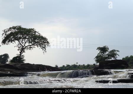 Bokeh-Aufnahme eines fließenden Wasserfalls mit selektivem Fokus und Baumhintergrund. Kleine Kinder baden im gefährlichen Wasserfall in Mirzapur, Indien w Stockfoto