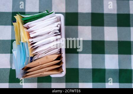 Weiß, rosa, blau, braun, Zuckertüten für Kaffee, Tee und Getränke auf grün weißem Schecktuch Stockfoto