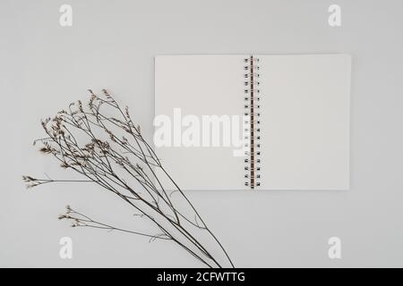 Leeres spiralgebundenes Skizzenbuch oder Tagebuch mit Limonium-Trockenblüte. Nachbau von Stationärmaterial. Draufsicht auf leeres Zeichenbuch auf weißem Hintergrund. Fl Stockfoto