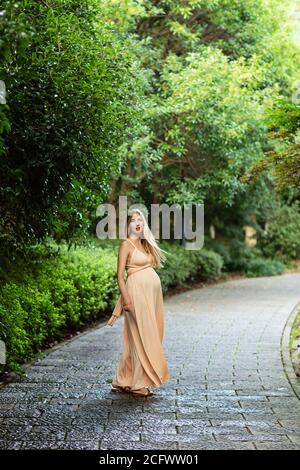 Schwangere Frau in Abendkleid steht im Freien im Sommer Park. Schwangerschaft, Mutterschaft, Vorbereitung und Erwartung Konzept. Schöne, zarte Stimmung Stockfoto