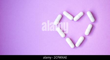 Das Herz aus Tabletten und Pillen auf violettem Hintergrund. Platz für Text kopieren. Stockfoto