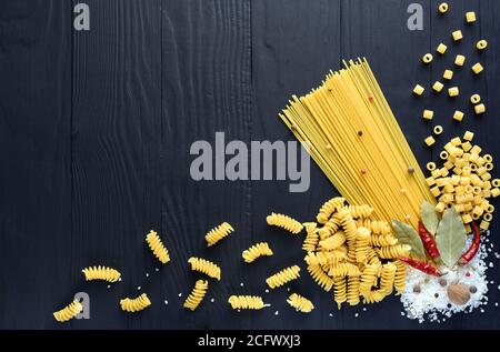 Verschiedene Vollkornpasta und farbenfroher Pfeffer auf dunklem Holzhintergrund. Italienisches Küchenkonzept mit Platz für Ihren Text. Stockfoto