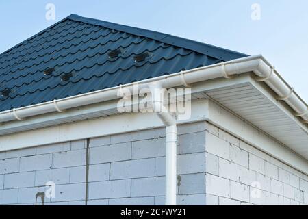 Neues Dach aus Metallfliesen mit weißer Regenrinne. SIP-Panelhauskonstruktion. Unvollendetes Gebäude. Stockfoto