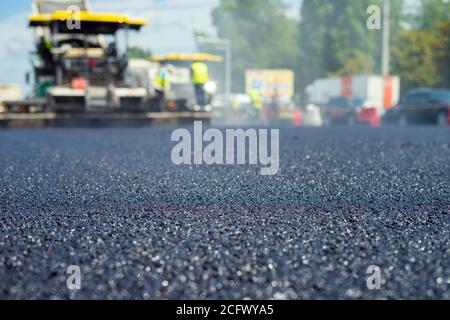 Nahaufnahme der neuen Asphaltstraße, auf der Spezialausrüstung arbeitet. Verschwommenes Foto von der Baustelle. Stockfoto