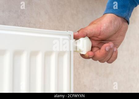 Männliche Hand regelt den Thermostat-Knopf auf dem weißen Heizkörper mit zu Hause eine kalte Jahreszeit. Stockfoto