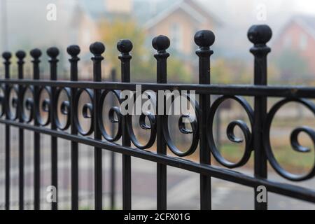 Schöner Metallzaun auf dem Hintergrund von Häusern im Nebel im Herbst. Leitplanke aus der Nähe. Stockfoto