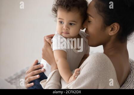 Fürsorgliche junge Mischlingsmutter kuscheln wenig biracial Baby. Stockfoto